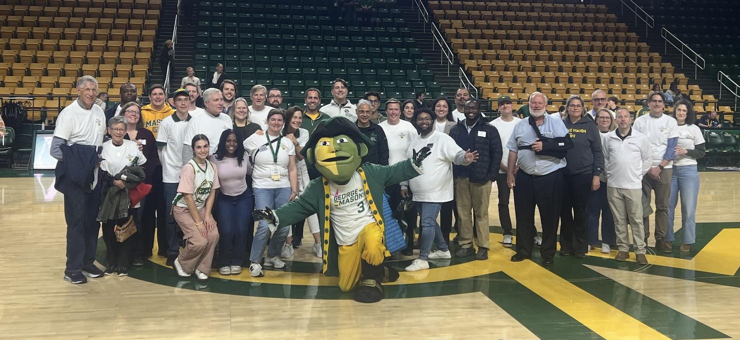 People gather on a basketball court for a picture with the George Mason University mascot