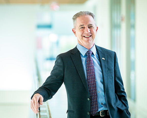 Ken Walsh stands in a white-painted building leaning on a railing.