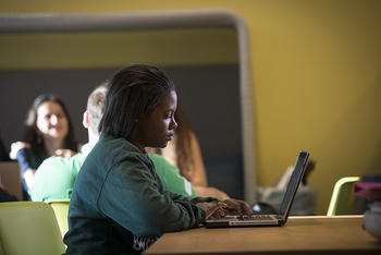 Person sits at a desk looking at a computer in the open study area of Fenwick library.