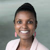 A black woman wears a pink blazer and has her hair in a bun